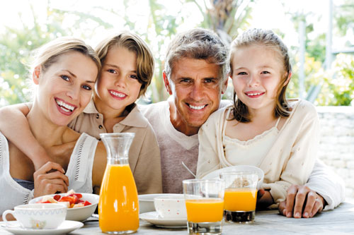 Family of four is eating breakfast outside.